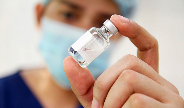 Profissional de saúde usando máscara e touca segurando uma ampola de vacina anti HPV.