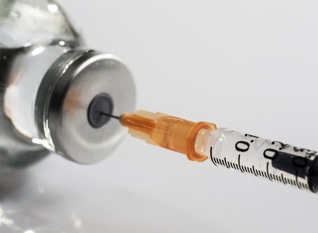 Na imagem uma agulha de vacina puxando o medicamento do frasco